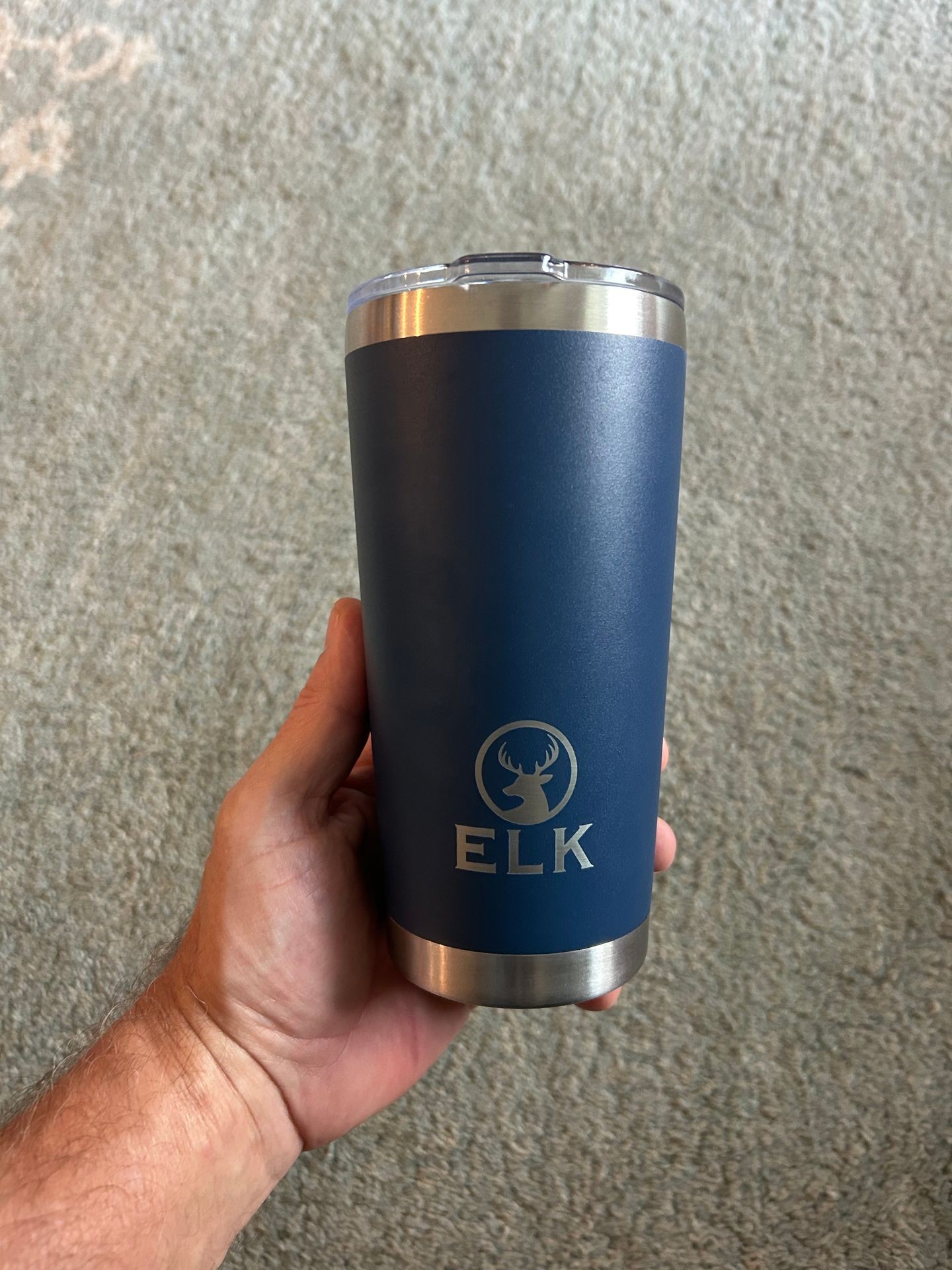 Hand holding a blue travel mug with silver base and lid, featuring an ELK logo.