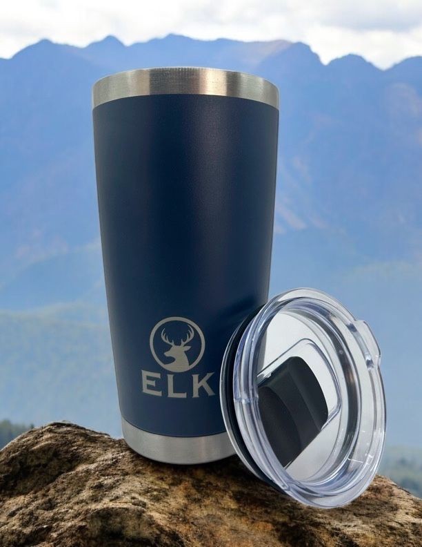 Stainless steel tumbler with logo and lid on a rock, mountainous background.